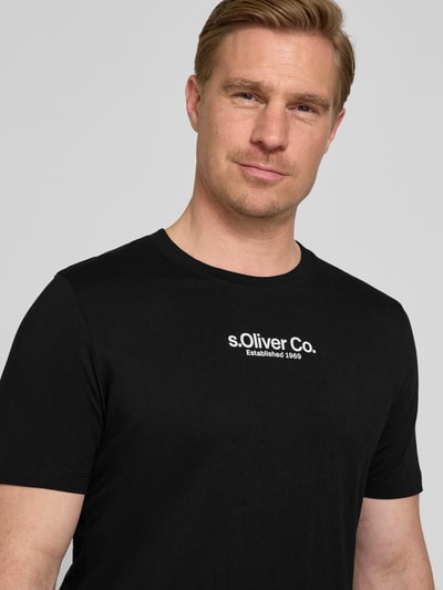 Męski model nosi Regular Fit T-Shirt aus reiner Baumwolle od s.Oliver RED LABEL, czarny, gładki, krótkie rękawy, jersey, napis z logo, ujęcie z przodu, zbliżenie na górną część ciała.
