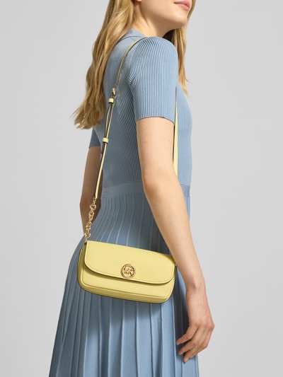 Modelka nosi żółtą Umhängetasche mit Label-Detail Modell 'NOLITA' od MICHAEL Michael Kors, widoczny regulowany pasek, faktura skóry, Szerokość w rozmiarze 1: 21 cm, głębokość 7 cm, długość 11 cm, długość paska 110 cm, zbliżenie na górną część ciała z przodu.