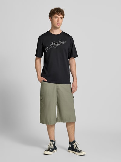 Männermodel trägt Oversized Fit T-Shirt mit Logo-Stitching von KARL KANI in Schwarz, Reine Baumwolle, Rundhalsausschnitt, Herren T-Shirt, Ganzkörperansicht von vorne, Rückenlänge bei Größe M: 72 cm.