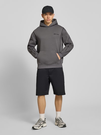 Männermodel trägt Hoodie mit Logo und Känguru-Tasche von REVIEW, Baumwoll-Mix, Regular-Fit, in Grau und Schwarz, Ganzkörperansicht von vorne.