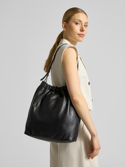Kobiece model prezentuje Hobo Bag mit Logo-Prägung Modell 'CLOUD' von LIEBESKIND BERLIN w kolorze czarnym, pasek na ramię, główna przegroda z zapięciem na magnes, szerokość w rozmiarze 1: 32 cm, długość w rozmiarze 1: 35 cm, głębokość w rozmiarze 1: 14 cm, długość paska na ramię w rozmiarze 1: 62 cm, widok całego ciała z przodu.