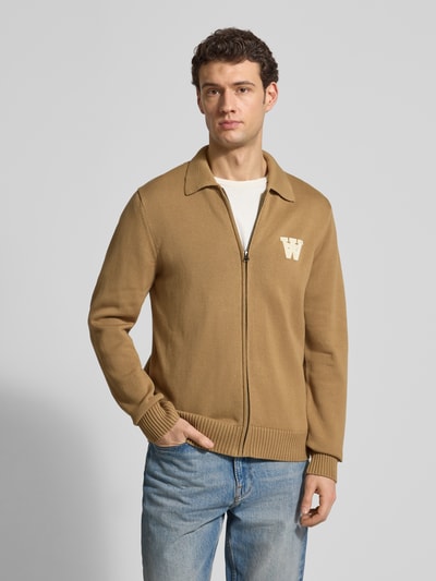 Męski model nosi Regular Fit Cardigan in Strick-Optik Modell 'Tay' od Wood Wood z bawełny, wykładany kołnierz, zamek błyskawiczny, wyhaftowane logo, elastyczne wykończenia, imitacja dzianiny, kolor beżowy, długość tyłu 70 cm w rozmiarze M, długość rękawów 70 cm w rozmiarze M, zdjęcie całej sylwetki z przodu.