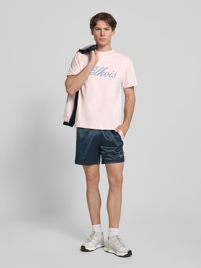 Męski model nosi T-Shirt mit Label-Print und Rundhalsausschnitt od BLKVIS z bawełny, krój regular fit, długość tyłu w rozmiarze M: 68 cm, widok całej sylwetki z przodu.