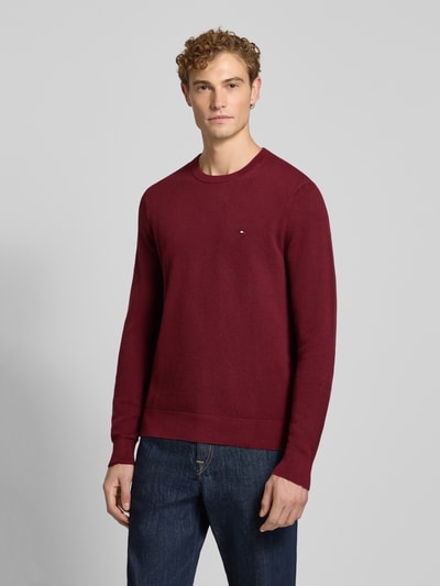 Męski model nosi Regular Fit Pullover aus reiner Baumwolle von Tommy Hilfiger, czerwony, prosty fason, widok całej sylwetki z przodu.