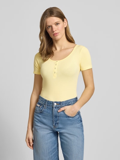 Modelka nosi damski t-shirt Slim Fit T-Shirt aus Baumwoll-Mix Modell 'KITTE' von Pieces, efekt: jednolity kolor, dekolt w łódkę, krótki rękaw, prążkowanie, mieszanka bawełny, jasny żółty, widok na górną część ciała z przodu.