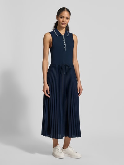 Kobiece modelka nosi Tailliertes Freizeitkleid aus Baumwoll-Mix od Tommy Hilfiger, granatowa unikatowa optyka, plisowany bawełniany strick, midi długość, krój slim fit, szerokie ramiączka, kolnierz polo, zapięcie na guziki, widok całej sylwetki z przodu.
