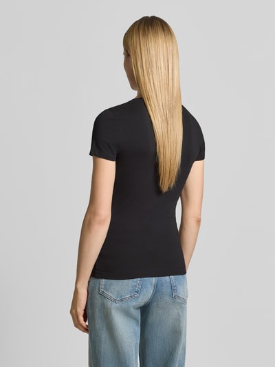 Frauenmodel trägt Damen T-Shirt mit U-Ausschnitt Modell 'SCRIPT' von Guess aus Baumwoll-Elasthan-Mix, körpernaher Schnitt, schwarzer Stoff, Label-Stitching, Rückenlänge bei Größe S 61 cm, Ganzkörperansicht Rückansicht.