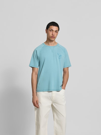 Männermodel trägt Regular Fit T-Shirt mit Logo-Print von MAISON KITSUNÉ in Hellblau aus reiner Bio-Baumwolle, Kurzärmelig, Rundhalsausschnitt, Rückenlänge 70 cm, Ganzkörperansicht von vorne.