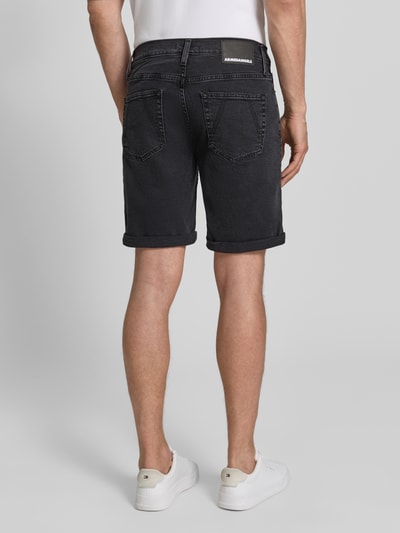 Männermodel trägt Slim Fit Jeansshorts aus Baumwoll-Mix Modell 'NAAILO' von Armedangels in Denim-Optik, Label-Patch, 5-Pocket-Design, Beinabschluss mit Umschlag, Ganzkörperansicht Rückansicht.