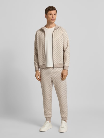 Männermodel trägt Sweatpants mit elastischem Bund Modell 'Eliton' von JOOP! Collection im Material-Mix mit Viskose-Anteil, Lockerer-Schnitt, hellbeige Muster, französische Eingrifftaschen, Gesäßtasche und Tunnelzug, Ganzkörperansicht von vorne.