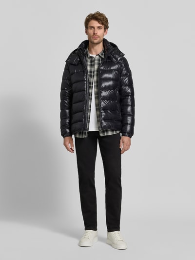 Männermodel trägt Steppjacke mit abnehmbarer Kapuze Modell 'FLORIAN' von Save The Duck in Schwarz mit Reißverschlusstaschen, Ganzkörperansicht von vorne.