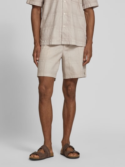 Männermodel trägt Tapered Chinoshorts aus reiner Baumwolle Modell 'SANDREW_6_SHORTS' von BOSS Orange, Optik: Unifarben, Struktur, Tunnelzug, Bundabschluss: elastisch, Beinabschluss mit Seitenschlitz, Farbe Beige, Ganzkörperansicht von vorne.