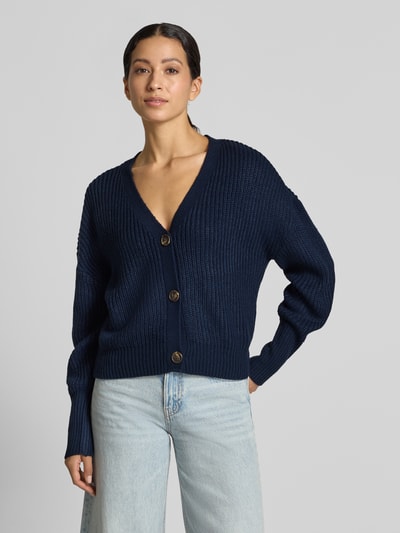 Modelka nosi ciemnogranatowy kardigan rozpinany z dekoltem w serek, model 'LEA' od VERO MODA, krój oversized, gładka faktura, widok z przodu, zdjęcie całej sylwetki.