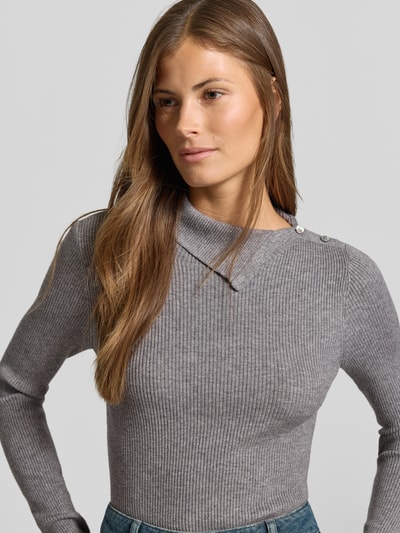 Modelka nosi sweter z dzianiny z mieszanki wiskozy od MYON, efekt prążkowania, wykładany kołnierz z listwą guzikową, krój slim fit, długość tyłu 58 cm, długość rękawów 64 cm, szary kolor, zbliżenie na górną część ciała.