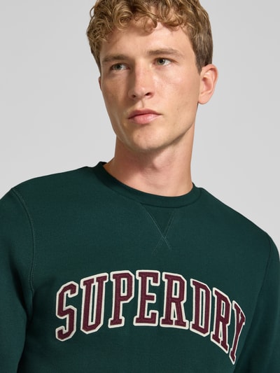 Männermodel trägt Regular Fit Sweatshirt aus Baumwoll-Mix mit Logo-Stickerei von Superdry, Rundhalsausschnitt, Nahaufnahme Oberkörper.