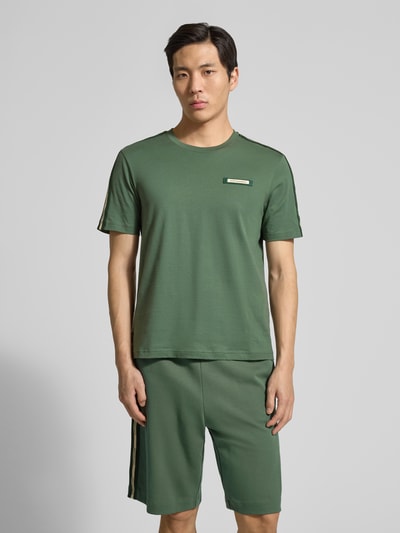 Męski model nosi Regular Fit T-Shirt mit Logo-Patch od EA7 Emporio Armani z bawełny, okrągły dekolt, kolor zielony, przód w pełnej sylwetce