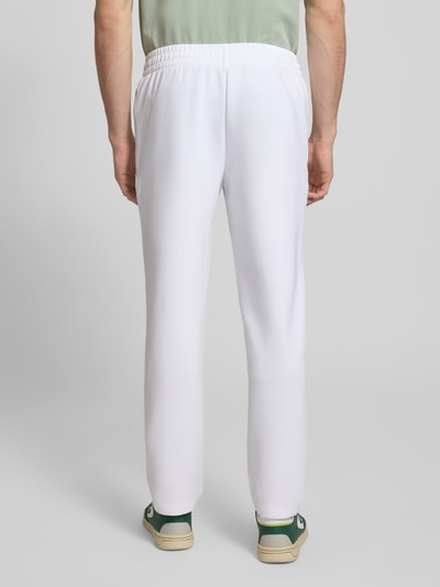 Männermodel trägt Tapered Sweatpants mit Baumwoll-Anteil von Lacoste Sport in Weiß, elastischer Bund, Reißverschlusstaschen, Ganzkörperansicht Rückansicht