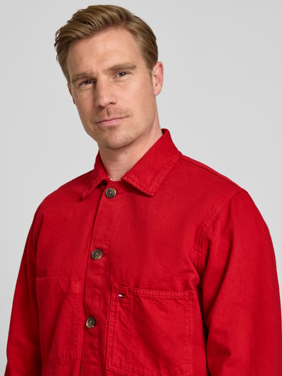 Männermodel trägt Regular Fit Hemdjacke aus reiner Baumwolle von Tommy Hilfiger in Unifarbe Rot, sichtbare Knopfleiste, Nahaufnahme Oberkörper.