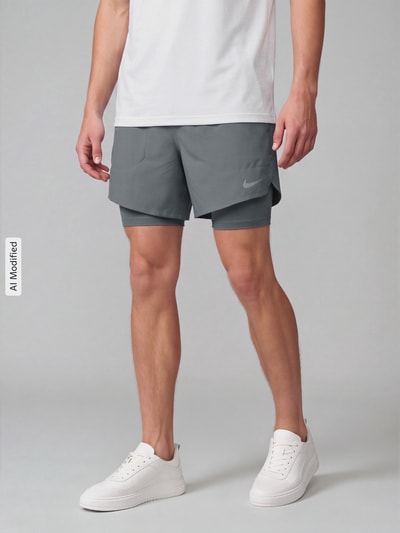 Mężczyzna nosi szare Regular Fit Sportshorts mit Dri-FIT-Technologie model 'STRIDE 5IN HYBRID' od Nike, Herren Sportshorts von Nike Training, całkowity widok z przodu, KI-modifiziertes Bild.