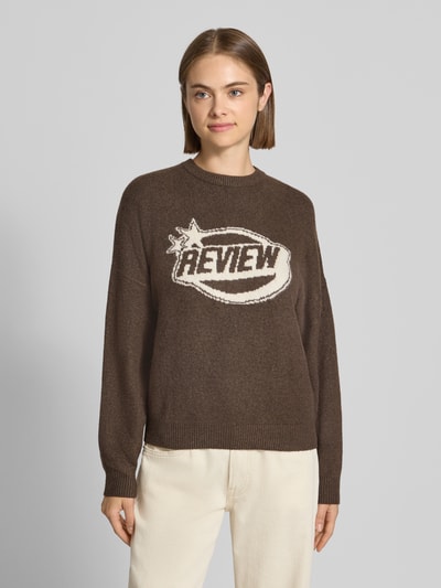Frauenmodel trägt Strickpullover mit Label-Print von REVIEW in Braun, lässiger Schnitt, Rundhalsausschnitt, Ganzkörperansicht von vorne.