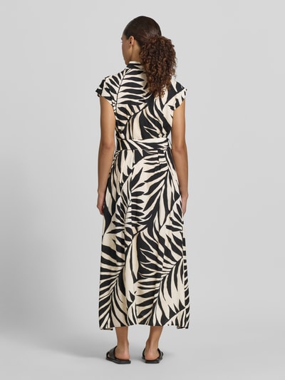Frauenmodel trägt Hemdblusenkleid aus Viskose mit Bindegürtel Modell 'APPLE' von Mango im schwarz-beigen Blättermuster, taillierter Schnitt, Midikleid mit Hemdblusenkragen und Kappärmeln, Rückenlänge 126 cm, Brustweite 44 cm, Ganzkörperansicht Rückansicht.