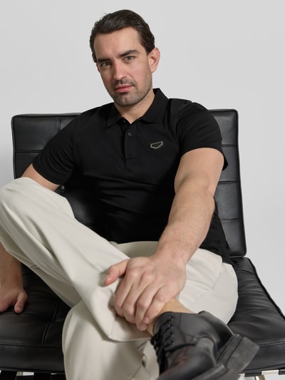Männermodel trägt Slim Fit Polo-Shirt mit Logo-Applikation von Antony Morato in Schwarz, reine Baumwolle, Logo am Oberkörper, Nahaufnahme Oberkörper.