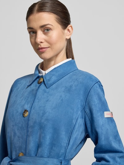 Frauenmodel trägt Trenchcoat mit Bindegürtel Modell 'CORDELIA' von Frieda & Freddies in Blau, Material-Mix mit Stretch, Nahaufnahme Oberkörper.
