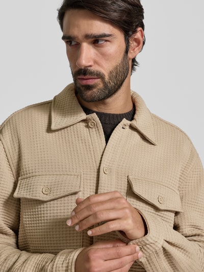 Männermodel trägt Hemdjacke mit knoopsluiting van MCNEAL in beige materiaalmix met viscose, borstzakken, los model, nahaufnahme oberkörper.