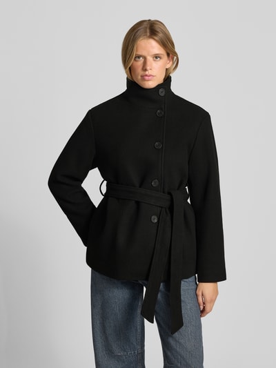 Frauenmodel trägt Jacke mit Stehkragen und Bindegürtel von REVIEW, Mieszanka materiałów z dodatkiem wiskozy, krój regular fit, listwa guzikowa, pasek wiązany, Długość tyłu w rozmiarze S: 70 cm, szerokość ramion w rozmiarze S: 57 cm, szerokość w klatce piersiowej w rozmiarze S: 46 cm, długość rękawów w rozmiarze S: 61 cm, czarny kolor, proste kształty, gładka tekstura, Ganzkörperansicht von vorne.