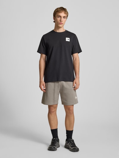 Męski model nosi Shorts mit Logo od The North Face z bawełnianej mieszanki, krój regular fit, elastyczny pas, szerokość w rozmiarze M: 41 cm, długość nogawki wewnętrznej: 18 cm, szare odcienie, gładka tekstura. Ganzkörperansicht von vorne.