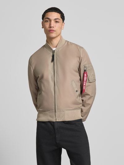 Męski model nosi Regular Fit Jacke mit Stehkragen od Alpha Industries, beżowa, gładka faktura, bomberka, kieszeń na rękawie, krój regular fit, zamek, elastyczne wykończenia, długość tyłu w rozmiarze M: 66 cm, szerokość ramion w rozmiarze M: 48 cm, szerokość klatki piersiowej w rozmiarze M: 54 cm, długość rękawa w rozmiarze M: 68 cm, całkowity widok z przodu