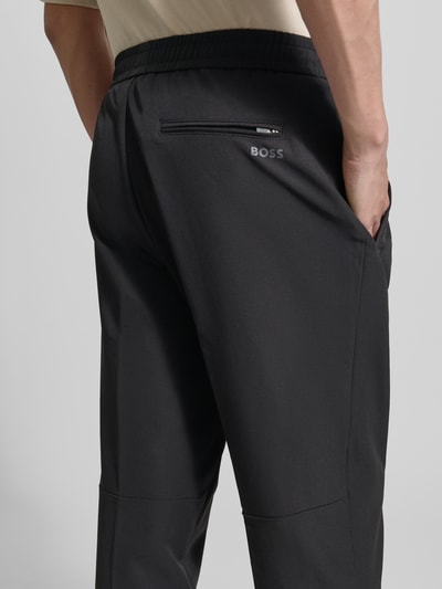 Männermodel trägt Tapered Fit Stoffhose mit Tunnelzug Modell 'T_FLEX' van BOSS Green, effen kleuren, tapered fit, mid waist, labelapplicatie, elastisch boord met tunnelkoord, zij-steekzakken, heren sweatpants, Ganzkörperansicht Rückansicht.