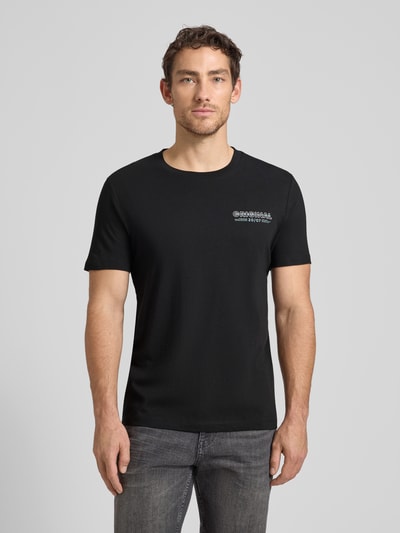 Männermodel trägt Regular Fit T-Shirt aus reiner Baumwolle von Tom Tailor Denim, unifarben schwarz, Rundhals, kurzarm, Label-Schriftzug, Ganzkörperansicht von vorne.