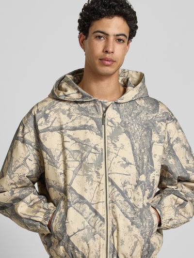 Männermodel trägt Jacke mit Kapuze und Logo von KARL KANI in Reine Baumwolle, Regular-Fit, Allover-Look, Reißverschluss, Nahaufnahme Oberkörper.