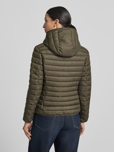 Frauenmodel trägt olivgrüne Steppjacke mit Zweiwege-Reißverschluss Modell 'DAISY' von Save The Duck, Quersteppung, Rückenansicht, Damen Steppjacke Slim Fit, Kapuze, Reißverschlusstaschen, strukturierte Oberfläche, Kontext: Länge 57 cm, Schulterbreite 44 cm, Brustweite 48 cm, Ärmellänge 60 cm, Ganzkörperansicht Rückansicht.