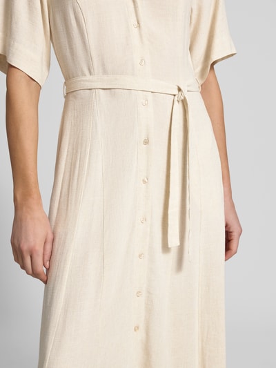 Kobieta nosi Regular Fit Leinenkleid mit V-Ausschnitt Modell 'VIVA' od Selected Femme, jasny beż, tkanina mieszanka wiskozy i lnu, guziki, pasek, krój regular fit, zbliżenie na górną część sukienki.