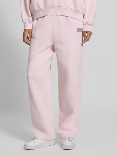 Frauenmodel trägt Sweatpants aus reiner Baumwolle mit Logo-Print Modell 'PLIZZY' von American Vintage in Hellrosa, gerade Passform, elastischer Bund, Seitentaschen, Baumwollstruktur, Ganzkörperansicht von vorne.