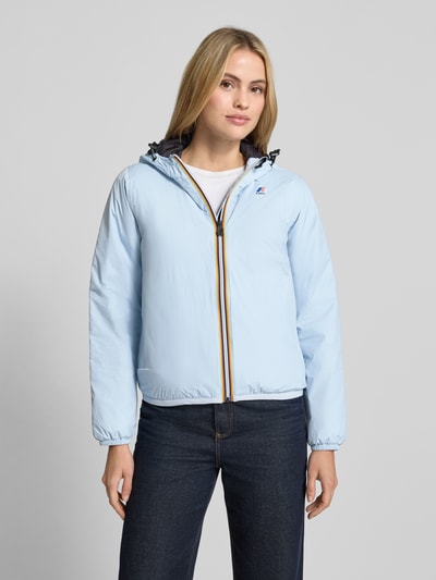 Modelka kobieca nosi jasnoniebieską Regular Fit Jacke mit Logo-Print Modell 'CLAUDETTE' od K-WAY, gładka faktura, długość pleców w rozmiarze S: 59 cm, szerokość ramion w rozmiarze S: 39 cm, szerokość klatki piersiowej w rozmiarze S: 51 cm, długość rękawa w rozmiarze S: 63 cm, z kapturem z tunelem i elastycznymi wykończeniami, widok całej sylwetki z przodu.