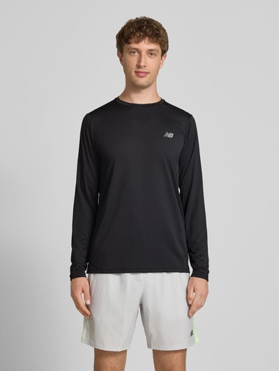 Männermodel trägt Funktionsshirt mit Rundhalsausschnitt und Logo von New Balance, Regular-Fit, Longsleeve, schwarze glatte Textur, Rückenlänge 72 cm bei Größe M, Ganzkörperansicht von vorne.