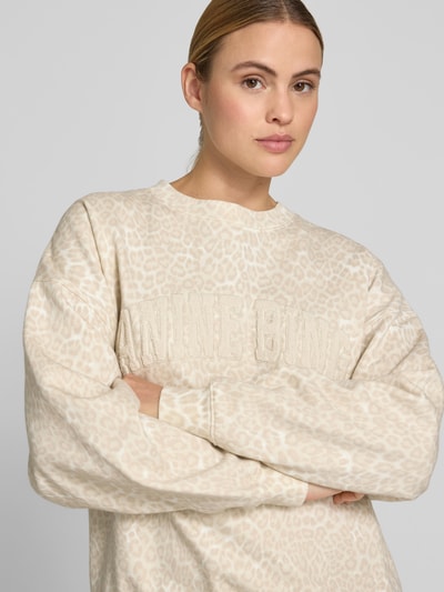Frauenmodel trägt Oversized Sweatshirt mit Logo-Detail von Anine Bing aus reiner Baumwolle im Oversized-Fit mit Allover-Animal-Print in Beige, elastische Abschlüsse, Rückenlänge bei Größe S: 64 cm, Nahaufnahme Oberkörper.