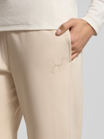 Frauenmodel trägt Sweatpants mit elastischem Bund Modell 'Twinka' von JOOP!, Material-Mix mit Modal-Anteil, Regular-Fit, Label-Stitching, Tunnelzug, creamfarben, glatte Textur, Nahaufnahme Oberkörper.