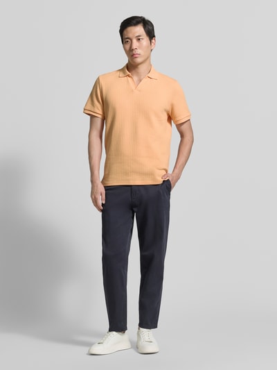 Männermodel trägt Regular Fit Strick-Poloshirt mit V-Ausschnitt von MCNEAL in Pfirsich, Baumwoll-Mix mit Stretch-Anteil, Ganzkörperansicht von vorne.