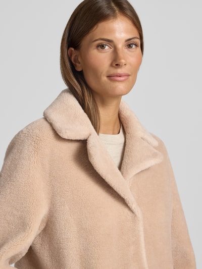 Frauenmodel trägt Wendemantel in Woll-Lammfell-Optik Modell 'VENUS' von OAKWOOD in Beige, Reverskragen, weiche Textur, Nahaufnahme Oberkörper. Lockere Passform, Eingrifftaschen, Rückenlänge 89 cm, Schulterbreite 44 cm, Brustweite 50 cm, Ärmellänge 62 cm.