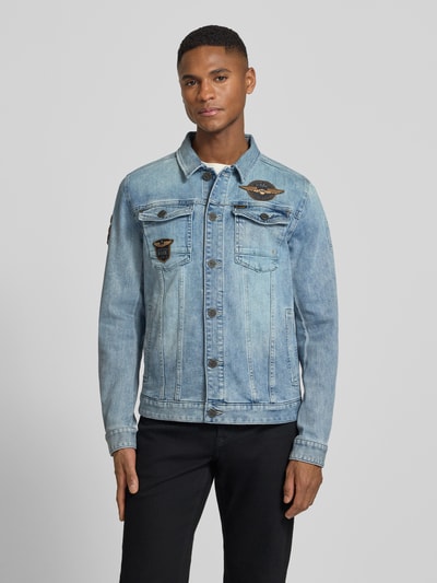 Mężczyzna model nosi Jeansjacke mit Label-Patches und Brusttaschen von PME Legend, jasnoniebieski bawełniany denim, prosty krój, naszywki, kieszenie, guzik, widok całej sylwetki z przodu, Szerokość w rozmiarze M: 53 cm, długość tyłu: 65 cm, szerokość ramion: 44 cm, długość rękawa: 67 cm.