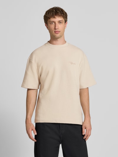 Männermodel trägt Oversized T-Shirt mit Strukturmuster und Label-Stitching von Pegador aus reiner Baumwolle in Beige, Rundhalsausschnitt, Ganzkörperansicht von vorne. Rückenlänge bei Größe M: 70 cm.