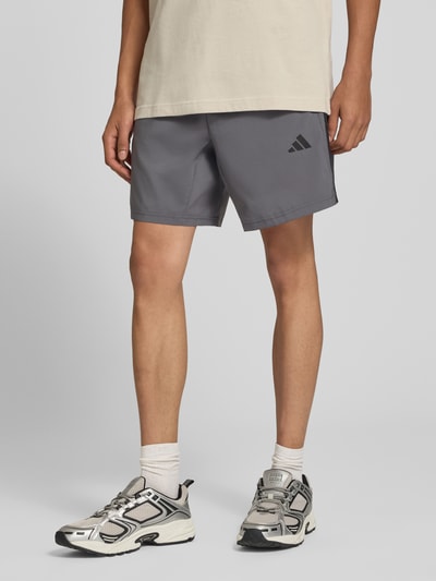 Männermodel trägt graue Regular Fit Sportshorts mit Logo-Print Modell 'WE BAS 3SWV SH' von adidas, Kontext: adidas Training, Nahaufnahme Oberschenkel.