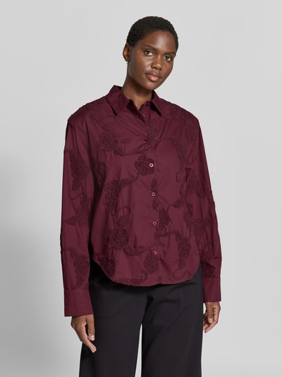 Frauenmodel trägt Oversized Hemdbluse aus reiner Baumwolle von ROTATE in Dunkelrot mit floralen Stickereien, Ganzkörperansicht von vorne. Rückenlänge 70 cm, Ärmellänge 63 cm, langärmliges Design, durchgehende Knopfleiste.