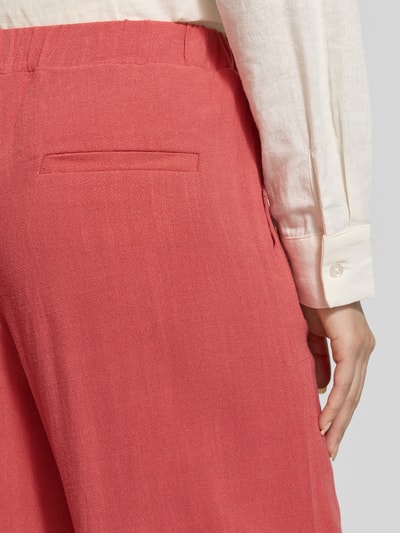 Frauenmodel trägt Stoffhose aus Viskose-Leinen-Mix mit elastischem Bund von Jake*s Casual in Koralle, Nahaufnahme Rückansicht. Relaxed-Fit mit Tunnelzug, breite Bundweite von 36 cm bei Größe 36, glatte Textur. Damen Stoffhose aus Viskose-Leinen-Mix mit Innenbeinlänge 100 cm.