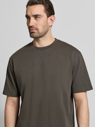 Männermodel trägt Oversized T-Shirt mit Rundhalsausschnitt von Lindbergh in Braun aus Reine Baumwolle, Label-Detail, Nahaufnahme Oberkörper.