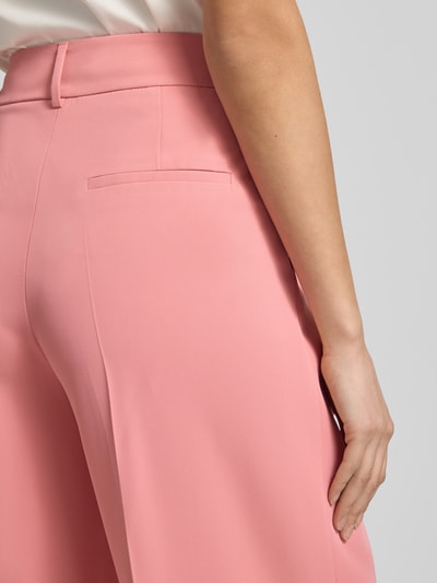 Kobiece modelka nosi Straight Fit Stoffhose mit Bügelfalten od Christian Berg Woman Selection, różowe spodnie materiałowe z kantami, kieszenie z tyłu, zapięcie na haftkę i zamek błyskawiczny, szerokość w rozmiarze 36: 39 cm, długość wewnętrzna nogawki w rozmiarze 36: 81 cm, detaliczne ujęcie tylnej części